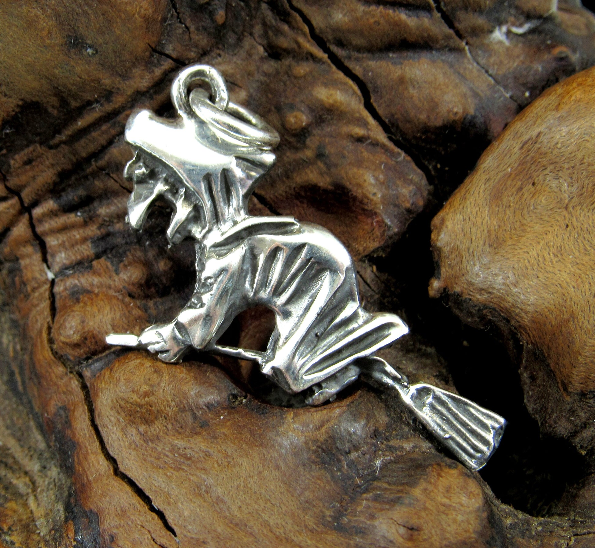 The handcrafted sterling silver witch flying on broom pendant features a wicked witch grasping a broom and flying west.